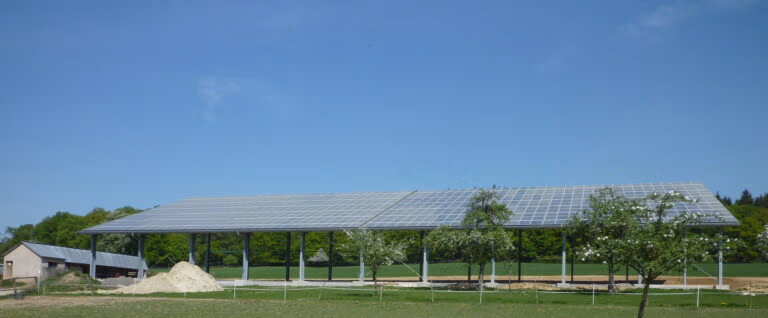 Große Solarzellenanlage in der Nähe von Schloss Hovestadt, auf einem hohen Metallrahmen inmitten von Bäumen und Gras.