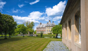 Schloss Hovestadt mit Teich und Liegewiese unter leicht bewölktem blauem Himmel.
