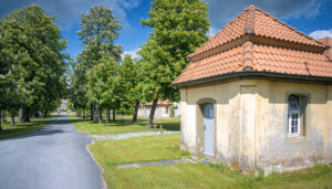 Kleines beiges Gebäude mit rotem Ziegeldach in der Nähe von Schloss Hovestadt an einer sonnigen, von Bäumen gesäumten Straße.