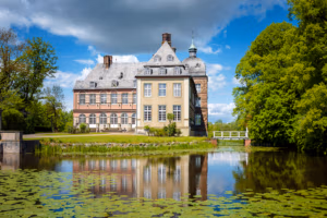 Schloss Hovestadt mit Backsteinfassade, das sich in einem Teich mit Seerosen und Bäumen spiegelt.