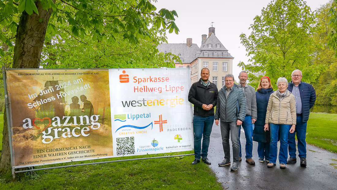 Sechs Personen stehen draußen vor den Bannern von Schloss Hovestadt und machen Werbung für eine Veranstaltung im Juni 2024.